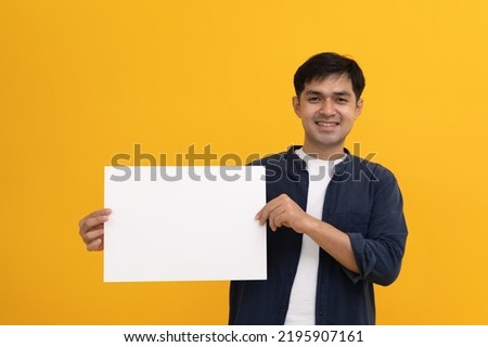 Happy man holding a large white paper blank for text or comments. blank white banner with copy space on blue studio background, mockup. Beautiful adolescent showing poster with place for your ad.