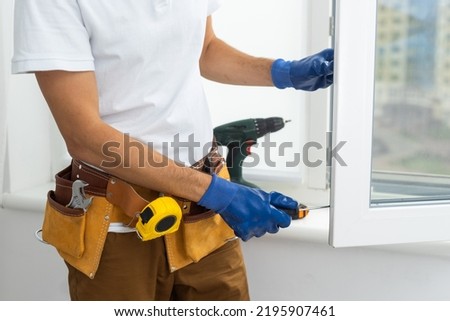 Master in gloves adjusting pvc windows with screwdriver closeup. Installation of plastic windows repair and maintenance concept. Royalty-Free Stock Photo #2195907461