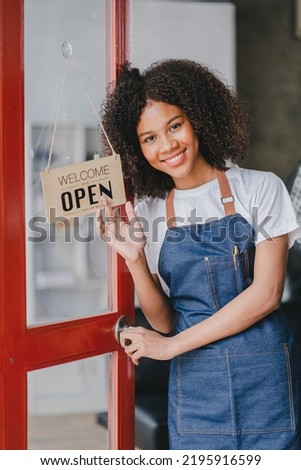 Small Business Owner, Young African American Woman
Turned on an open sign standing at the entrance to a coffee shop. Ready to open the door to observe customers, SME entrepreneurs
