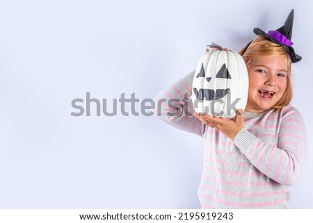 Happy Halloween holiday greeting card background. Happy cute european blonde girl in striped sweater with witch costume hat and jack carved decor pumpkin on white background copy space for text