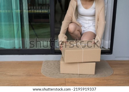 A woman goes out to pick up parcels on the front porch. The parcel was delivered and placed on the carpet in front of the house. Royalty-Free Stock Photo #2195919337