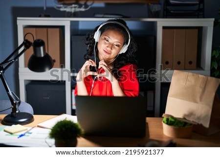 Young asian woman working at the office with laptop at night smiling in love doing heart symbol shape with hands. romantic concept. 