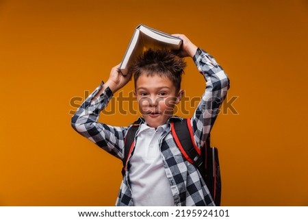 Portrait of a schoolboy boy holding a book over his head, with a bag, backpack, isolated on a yellow background.back to school