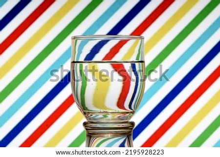 Optical illusion created by refracting light with a glass of water and colored diagonal lines Royalty-Free Stock Photo #2195928223