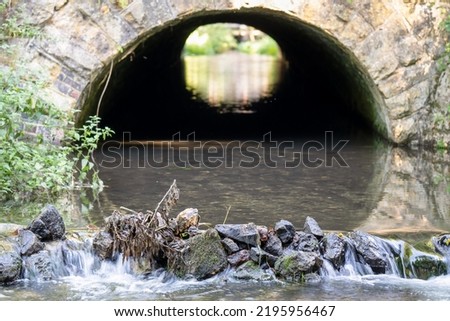 close-up of a chalk stream river flowing out of a stone arched tunnel and over a small stone waterfall
