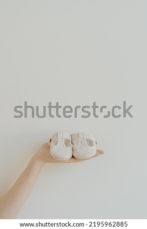 Hand hold pair of small cute newborn baby sandals shoes on white background. Minimal gender neutral baby fashion composition