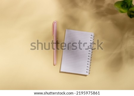 Mockup with blank clean notebook with copy space. Hard sunlight and shadows on a beige background with summer flowers. Template for business layout. Top view, flat lay