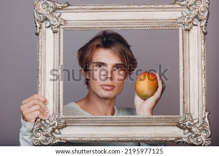 Millenial young man artist with blonde hair on gilded picture frame portrait with apple.