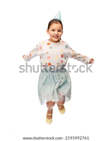 birthday, childhood and people concept - portrait of smiling little girl in dress and party hat jumping over white background