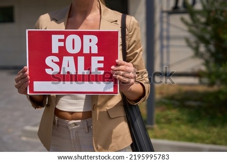 Female realtor stands with sign in her hands for sale