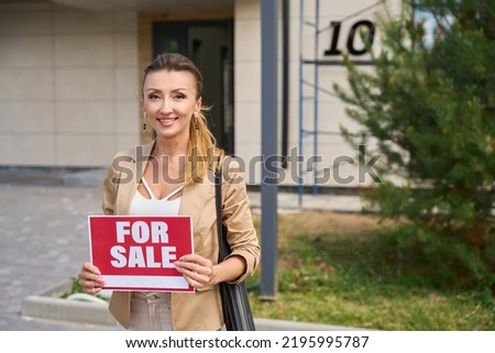 Woman realtor stands with sign in her hands for sale