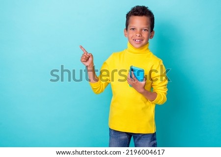 Photo of positive funny boy arm hold telephone direct demonstrate empty space ad offer cool device gadget isolated on cyan color background