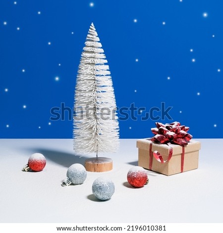 Beautiful Christmas or New Year banner. Toy Christmas tree, gift box with red bow and Christmas baubles on blue background with snow falling on the background
