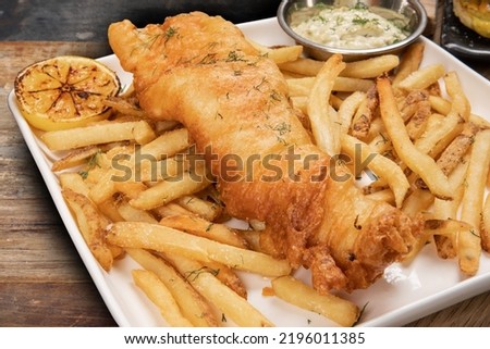 closeup of traditional British pub fare, a crispy battered haddock filet with french fried chips and tartar sauce