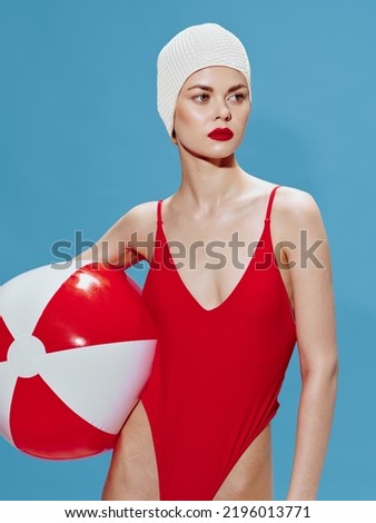 A spectacular model in a swimming cap with a ball poses on a blue background