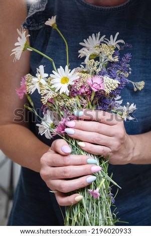 a young woman with a beautiful summer manicure holds a bouquet of wild flowers