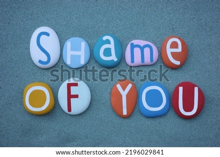 Shame of you, creative multi colored stone letters phrase composed over green sand