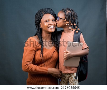 An african Nigerian mother, teacher or guardian hugging her child or daughter while the girl kisses her on the cheek and also holding an education smart tablet