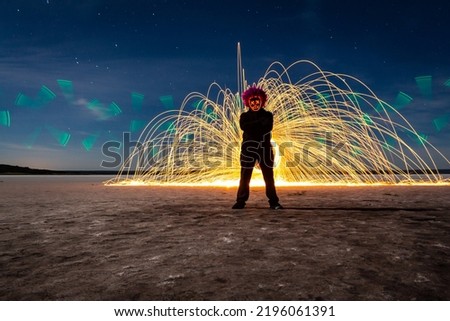 Silhouette of a masked man standing in front of a glowing steel wall. Long exposure photography.
