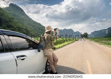 side view of young woman traveler taking pictures of mountains in the sky on the road beside the car