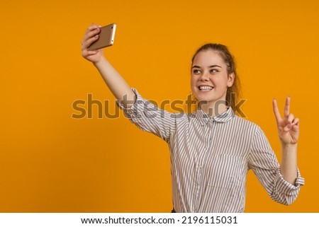 cheerful teen girl in a shirt photographs herself on a smartphone on a colored background