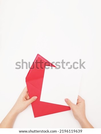  Female hands with pink envelope and blank card. Woman holding envelope square invitation card mockup on white background. Top view with copy space. Template for branding and advertising              