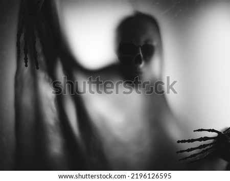 Horror skeleton or grim reaper behind the matte glass. Halloween festival concept.Blurred picture