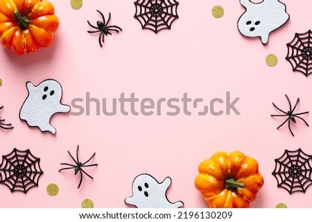 Happy Halloween holiday concept. Halloween decorations, pumpkins, ghosts, spiders on pastel pink background. Halloween party greeting card mockup with copy space. Flat lay, top view, overhead.