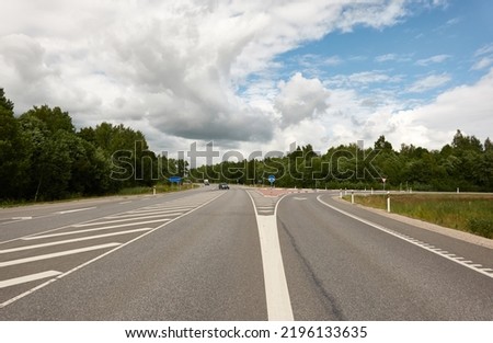 Empty highway through the forest on a sunny day. Asphalt road surface marking. Estonia, Europe. Transportation, traffic law, wanderlust, remote places, summer vacations concepts