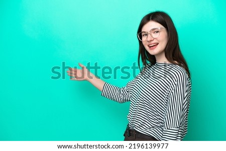 Young Russian woman isolated on green background extending hands to the side for inviting to come
