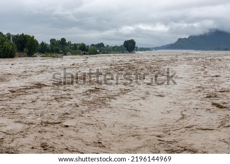 A rapid stream of muddy rain water entering in the river Royalty-Free Stock Photo #2196144969