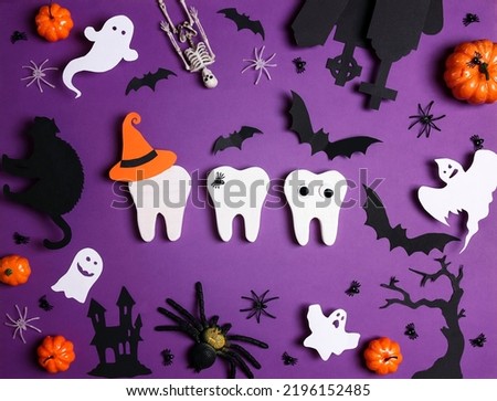 White teeth with Halloween decorations on purple background. Dentist Halloween concept. Top view, flat lay.