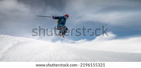 A sportsman skier in ski equipment jumps down a steep snowy slope of a mountain against the backdrop of a blue sky and snow-capped mountains. Winter risky sports, courage and speed concept Royalty-Free Stock Photo #2196155321