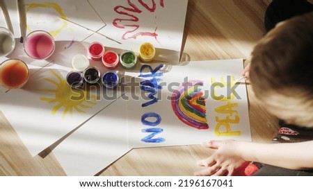 Child painting with acrylic paint paper. Hand writes slogan peace with brush, using watercolor paint on white paper.