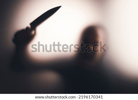 Horror, halloween background - Shadowy figure behind glass holding a knife