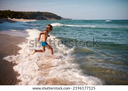 eight year old boy with long blond hair joyfully runs to swim in the sea.
