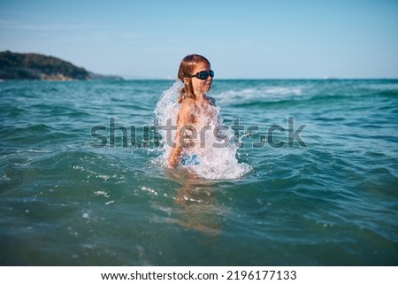 boy of 8 years old swims in the sea in blue swimming goggles in the evening