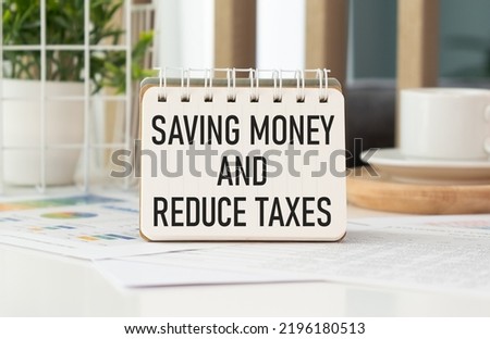 Business concept. On a gray surface is a pack of dollars on which there is a clip with torn paper and the inscription - Saving Money and Reduce Taxes.