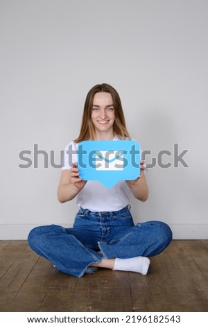 A beautiful caucasian girl sits on the floor and holds a icon messages in messenger in front