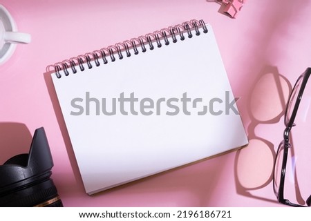Blank notebook, SLR camera with glasses on desktop top view on pink background. Learning photography, blogging concept.