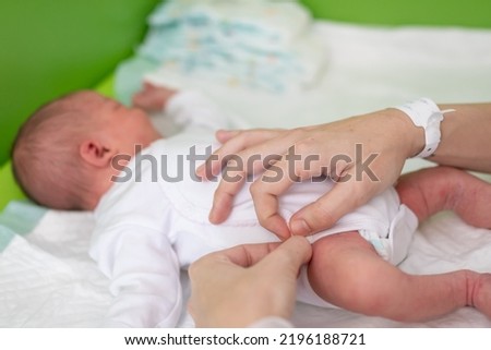 The hands of a mother who has just given birth in the maternity hospital puts a bodysuit on her newborn baby after bathing and changing his diaper. newborn baby health care Royalty-Free Stock Photo #2196188721