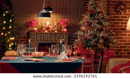 Empty traditional Christmas dinner table inside decorated living room with holiday garlands and dinnerware. Interior of traditional and authentic season cozy setting celebrating religious event. Royalty-Free Stock Photo #2196193765