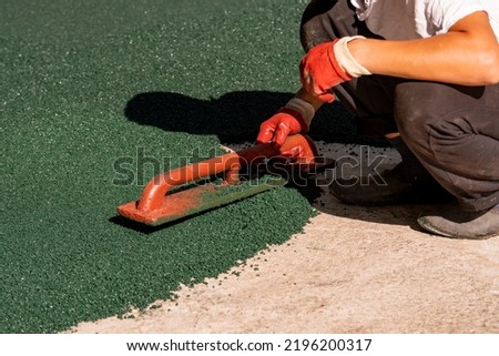 A worker applies a rubber coating to a concrete surface prepared for coating. Rubber crumb obtained in the process of recycling used car tires is used for flooring sports and playgrounds. Royalty-Free Stock Photo #2196200317