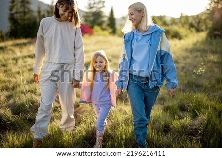 Two women walk with little girl, happily spending summer time on nature. Homosexual family with a kid travel in mountains Royalty-Free Stock Photo #2196216411