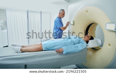CT scan technologist overlooking woman patient in CT scanner during settings on Computed Tomography scanner Royalty-Free Stock Photo #2196221505