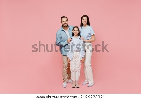 Full size young happy caucasian smiling fun parents mom dad with child kid daughter teen girl in blue clothes look camera hug cuddle isolated on plain pastel light pink background. Family day concept