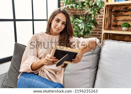 Young hispanic woman smiling confident holding picture at home
