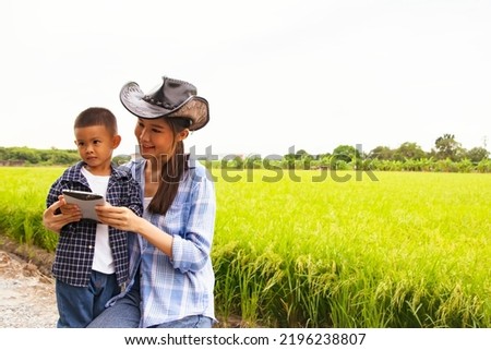 Family portrait happy asian farmer mother and son teach cute son use tablet at outdoor paddy field caring share touch screen tablet enjoy watching video.
