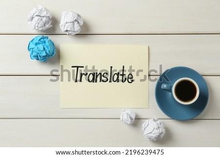 Card with word Translate, crumpled paper balls and cup of coffee on white wooden table, flat lay