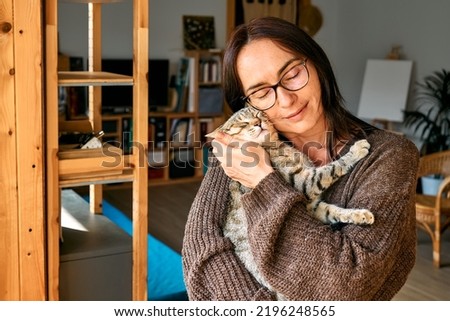 Middle-aged woman hugging cute tabby cat in indoor scene. Human-animal relationships. Funny home pet. Homeless pets.